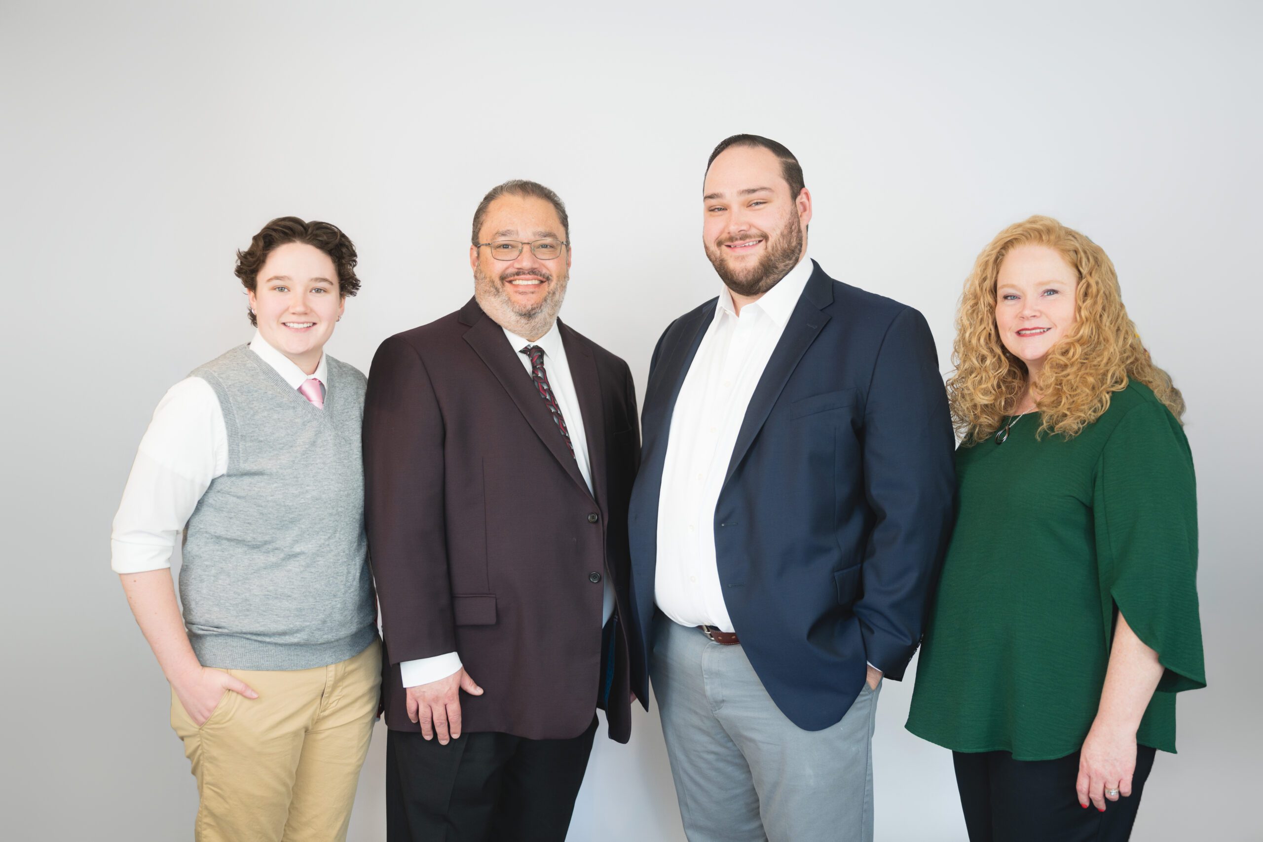 Four people stand side by side against a plain background, dressed in business casual attire, smiling at the camera.